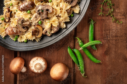 Mushroom and cheese pasta. Farfalle with cremini and green peas, shot from the top with ingredients on a dark rustic wooden background with a place for text