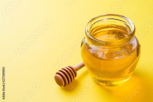 jar of liquid honey and a stick on yellow background. Copy space.