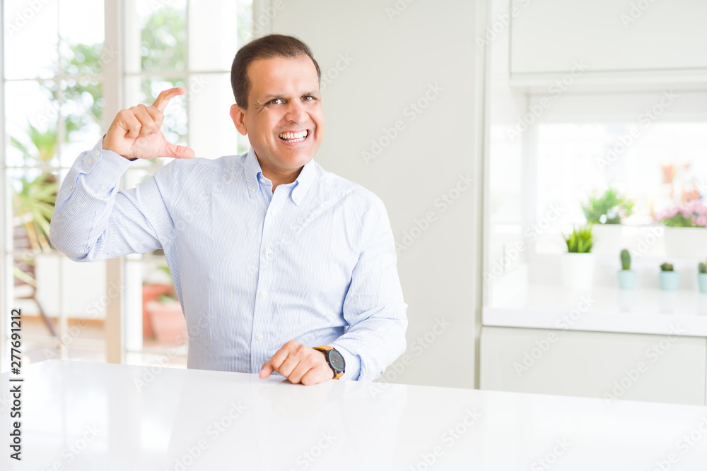Middle age man sitting at home smiling and confident gesturing with hand doing size sign with fingers while looking and the camera. Measure concept. Middle age man sitting at home smiling and confident gesturing with hand doing size sign with fingers while looking and the camera. Measure concept.