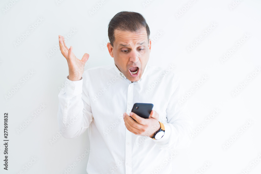 Middle age man using smartphone over white wall very happy and excited, winner expression celebrating victory screaming with big smile and raised hands Middle age man using smartphone over white wall very happy and excited, winner expression celebrating victory screaming with big smile and raised hands
