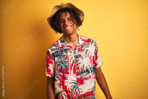 Afro american man with dreadlocks wearing floral shirt and hat over isolated yellow background with a happy and cool smile on face. Lucky person.