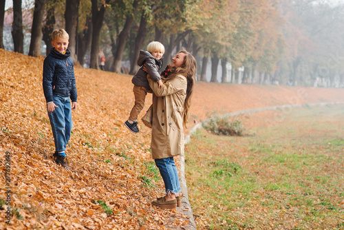 Happy family enjoing autumn day. Young mother and children on autumn walk in park. Cute brothers having fun with mom. Autumn weather, holidays, and fashion