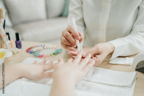 female Asian manicurist using portable pen shape by electric drill on customer finger. beauty art home service concept. close up beautician doing manicure file polish buffing for woman customer