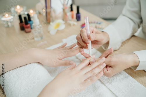 unrecognized woman worker in home service holding female client hands applying nourishing oil on cuticles. beautician doing manicure work for lady customer on wooden table. close up vie concept.