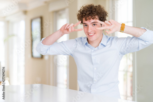 Young business man with curly read head Doing peace symbol with fingers over face, smiling cheerful showing victory