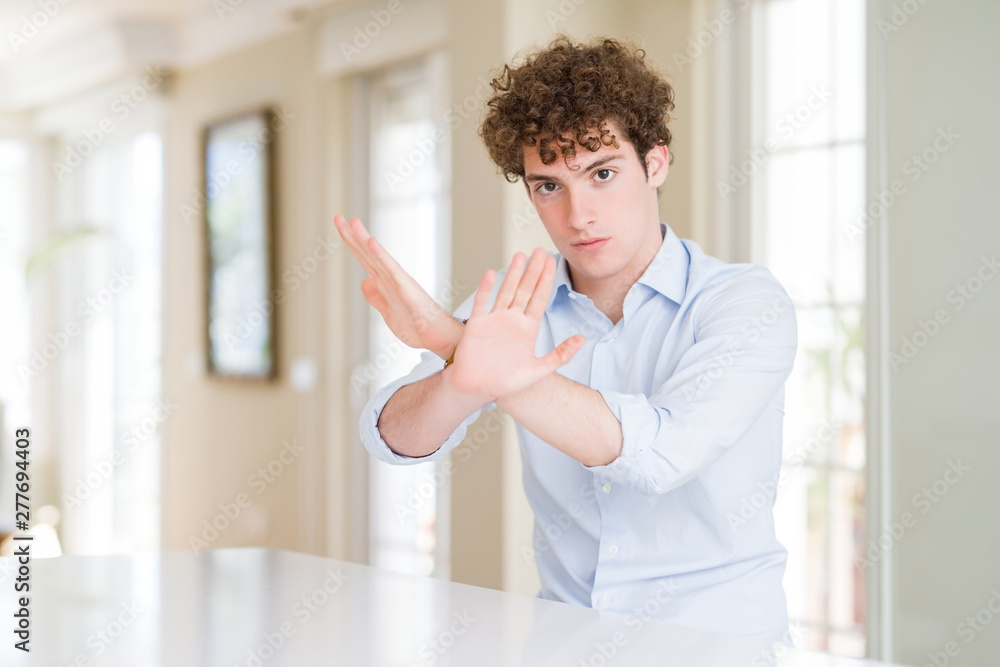Young business man with curly read head Rejection expression crossing arms and palms doing negative sign, angry face
