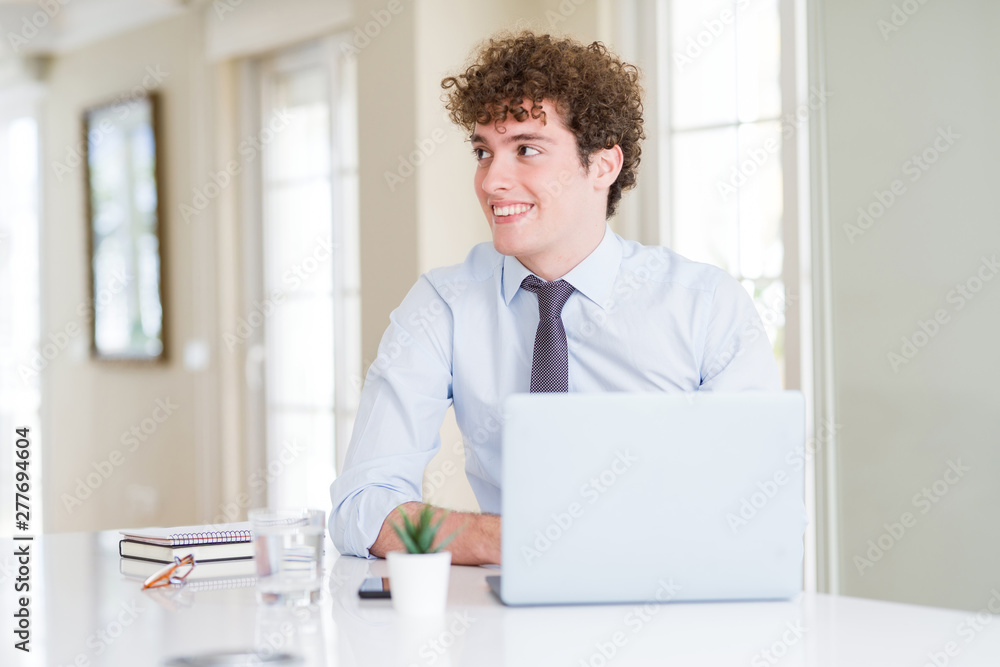 Young business man working with computer laptop at the office looking away to side with smile on face, natural expression. Laughing confident.