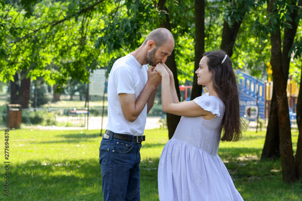 Husband kissing touchingly his pregnant wife's hands in the park on a sunny day in summer. An emotional portrait of happy couple on the third semester expecting baby's arrival Husband kissing touchingly his pregnant wife's hands in the park on a sunny day in summer. An emotional portrait of happy couple on the third semester expecting baby's arrival