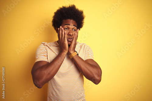 American man with afro hair wearing striped t-shirt standing over isolated yellow background Tired hands covering face, depression and sadness, upset and irritated for problem © Krakenimages.com