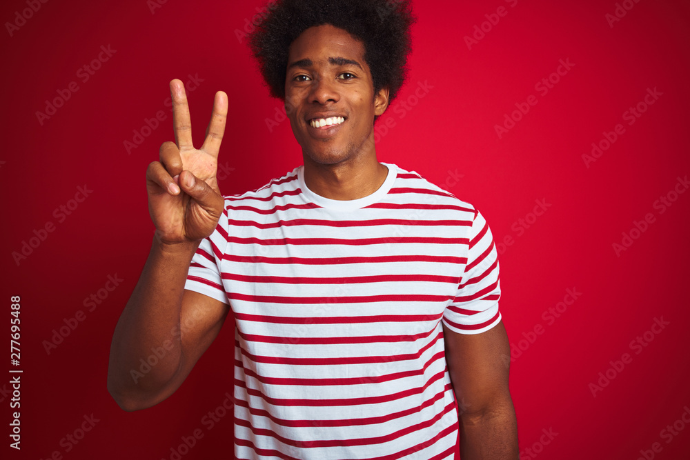Young african american man with afro hair wearing striped t-shirt over isolated red background showing and pointing up with fingers number two while smiling confident and happy. Young african american man with afro hair wearing striped t-shirt over isolated red background showing and pointing up with fingers number two while smiling confident and happy.