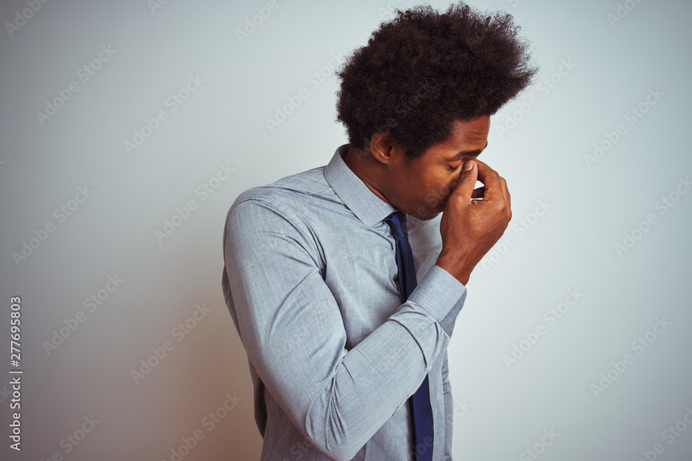 American business man with afro hair wearing shirt and tie over isolated white background tired rubbing nose and eyes feeling fatigue and headache. Stress and frustration concept. American business man with afro hair wearing shirt and tie over isolated white background tired rubbing nose and eyes feeling fatigue and headache. Stress and frustration concept.
