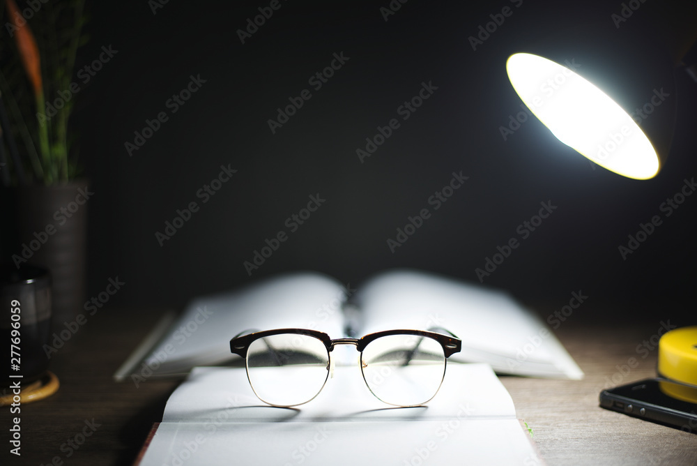 Reading table at night, With books, glasses, lamps, Focus on glasses, Education concept. - obrazy, fototapety, plakaty 