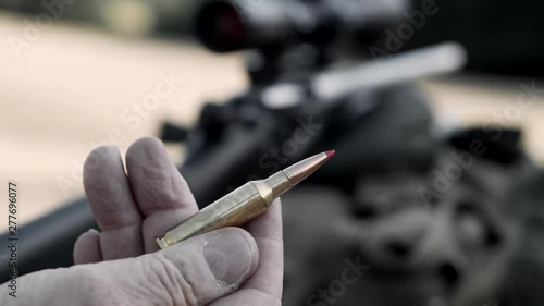 Bullet with sniper rifle on background. Hand take a bullet slowmotion.