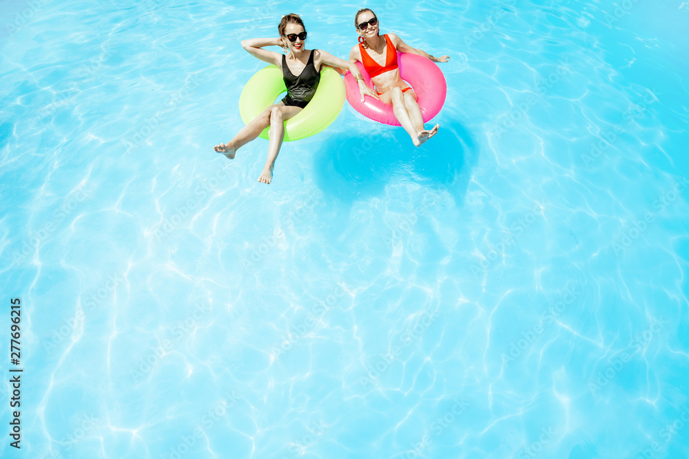 Two women swimming on the inflatable rings, relaxing in the water pool outdoors during the summer time, View from above