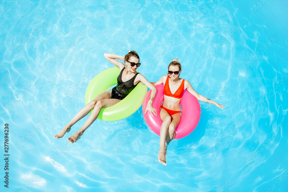 Two women swimming on the inflatable rings, relaxing in the water pool outdoors during the summer time, View from above