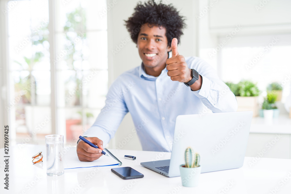 African American business man working writing on notebook happy with big smile doing ok sign, thumb up with fingers, excellent sign African American business man working writing on notebook happy with big smile doing ok sign, thumb up with fingers, excellent sign