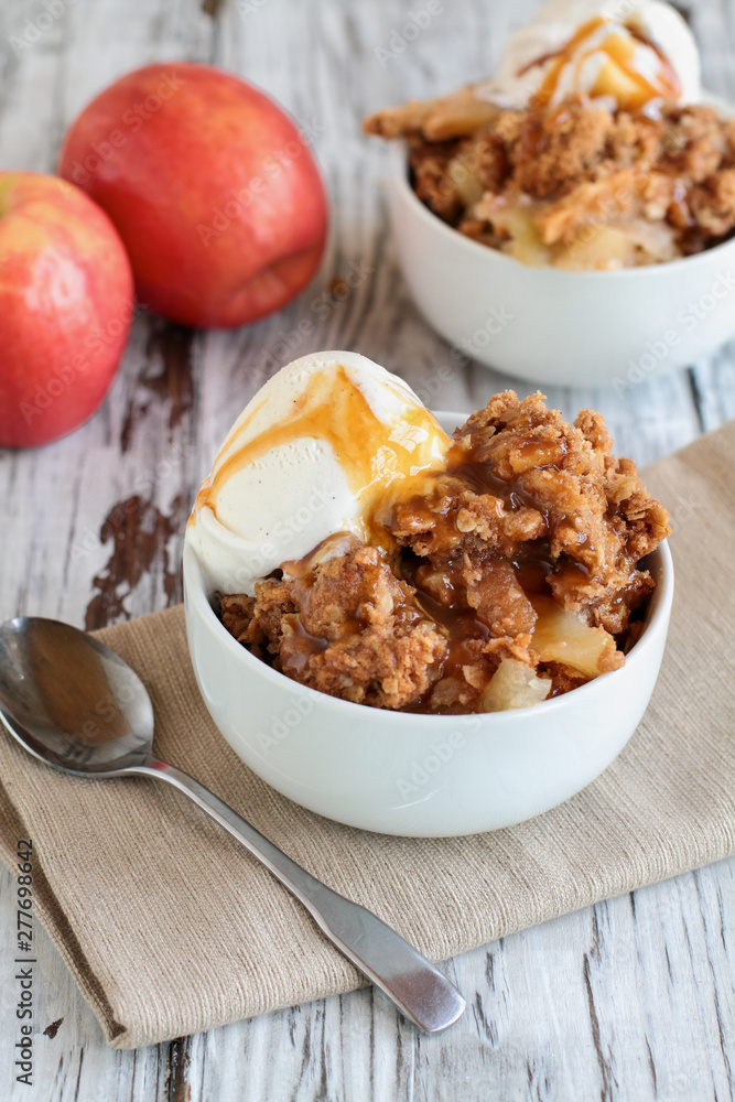 Fresh hot homemade apple crisp or crumble with crunchy streusel topping topped with vanilla bean ice cream and Caramel Sauce. Selective focus with blurred background Fresh hot homemade apple crisp or crumble with crunchy streusel topping topped with vanilla bean ice cream and Caramel Sauce. Selective focus with blurred background