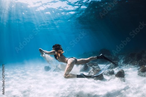 Woman freediver swim underwater over sandy bottom with sand in hands