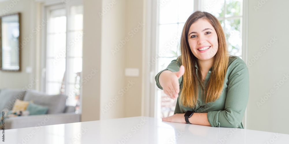 Beautiful young woman at home smiling friendly offering handshake as greeting and welcoming. Successful business. Beautiful young woman at home smiling friendly offering handshake as greeting and welcoming. Successful business.