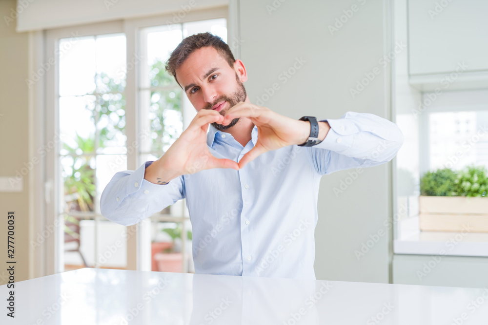Handsome business man smiling in love showing heart symbol and shape with hands. Romantic concept.