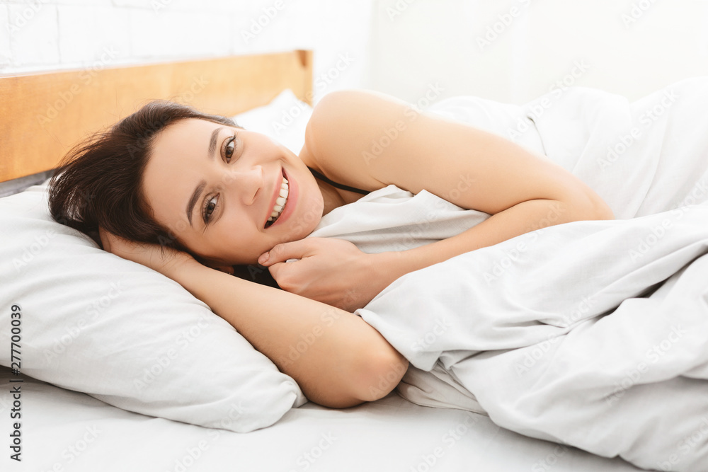 Positive woman smiling at camera, lying in bed after good sleep Positive woman smiling at camera, lying in bed after good sleep