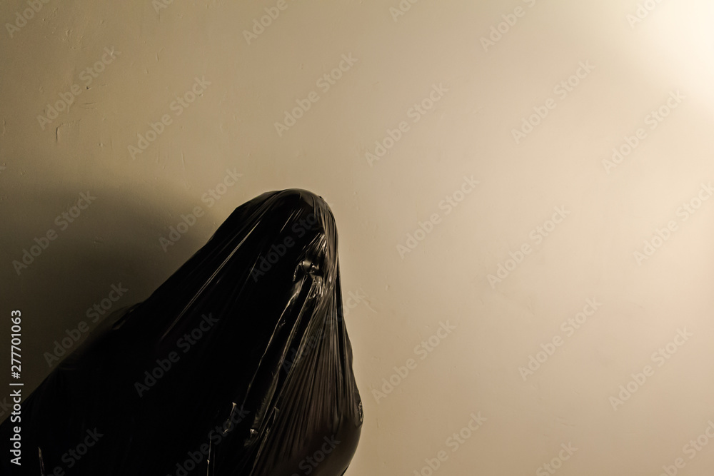 Concept Image of Human Figure Covered in Black Plastic Bag and Screaming.  Copy Space for Suffocation and Fear. Dark Stock Photo.