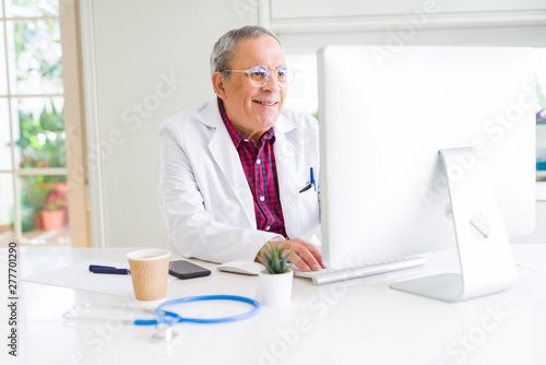 Senior doctor man at the clinic working with computer and smiling