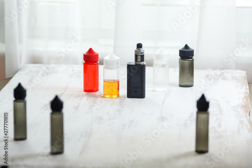 Vape objects. Electronic cigarette and jars with e-liquid on a light wooden table.