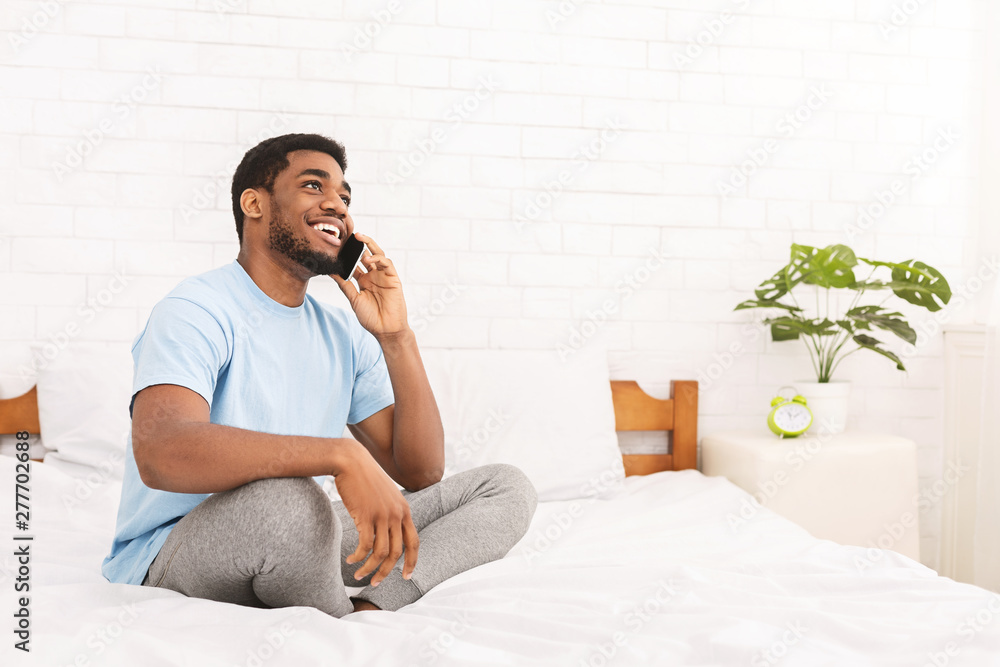 Cheerful african-american guy talking on phone in bed Cheerful african-american guy talking on phone in bed