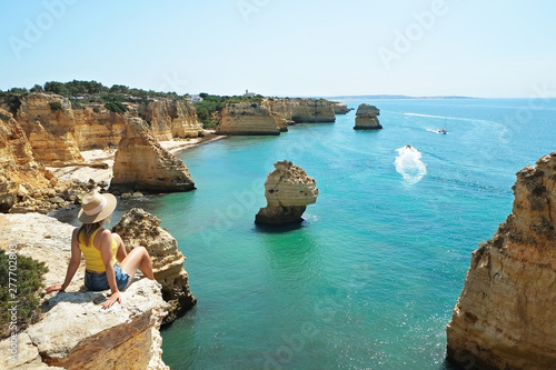 Young beautiful woman enjoying the panoramic top view of rocky beaches with cliffs somwhere, somwhere in Algarve, Portugal. Atlantic ocean shore background. Copy space for text.
