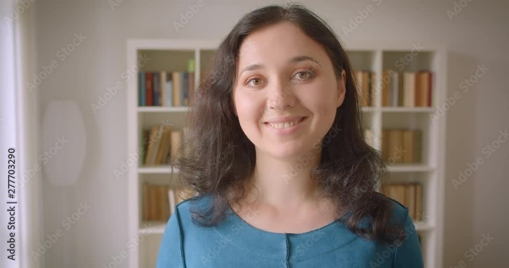 Closeup portrait of young pretty caucasian female student looking at camera smiling happily in the college library indoors Closeup portrait of young pretty caucasian female student looking at camera smiling happily in the college library indoors