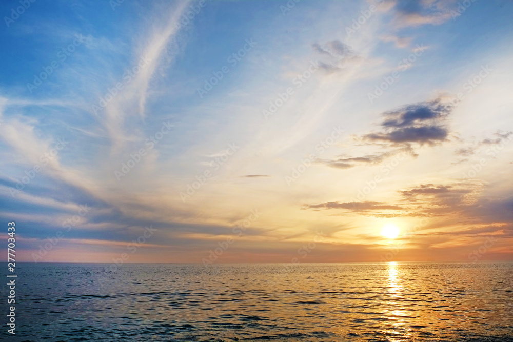 Beautiful seascape of sun setting over calm azure water with wind patterns and clear blue orange gradient sky without clouds. Ocean view with horizon, background with a lot of copy space for text.