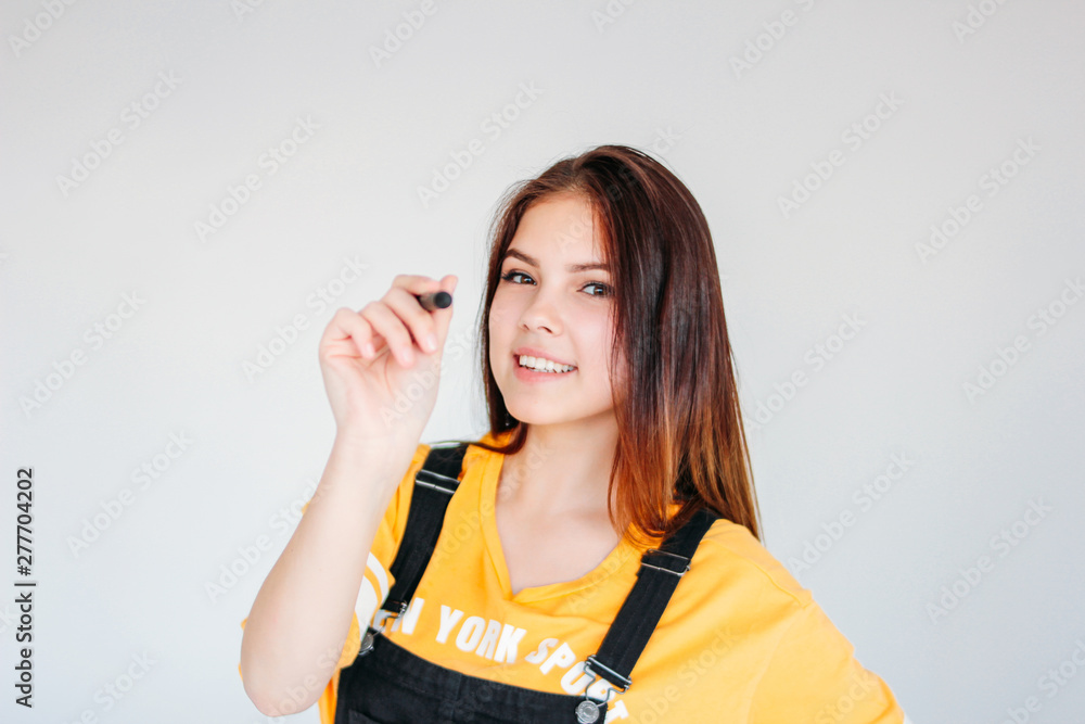 Young smiling girl student worker with dark long hair in yellow t-shirt with graphic pen in hand, isolated on grey background Young smiling girl student worker with dark long hair in yellow t-shirt with graphic pen in hand, isolated on grey background