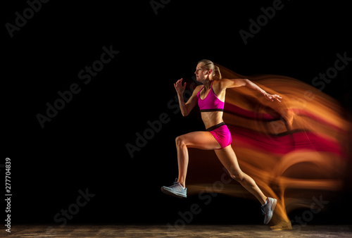 Professional female relay racer training isolated on black studio background in mixed light. Woman in sportsuit practicing in running. Healthy lifestyle  sport  workout  motion  action concept.