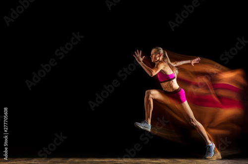 Professional female relay racer training isolated on black studio background in mixed light. Woman in sportsuit practicing in running. Healthy lifestyle, sport, workout, motion, action concept.