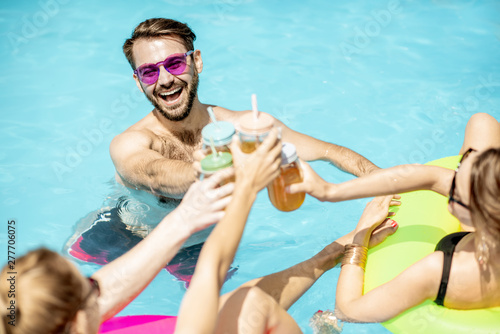 Photography Group of a happy friends having fun with drinks while swimming in the water pool