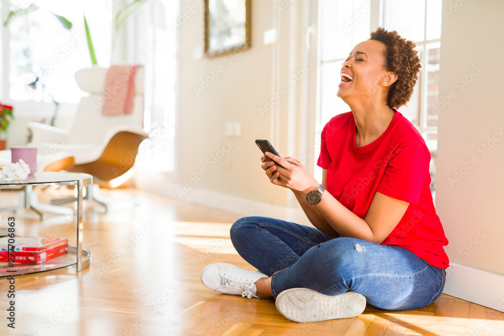 Obraz premium Beautiful young african american woman sitting on the floor using smartphone smiling