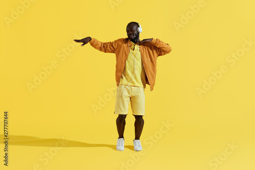 Fototapeta Naklejka Na Ścianę i Meble -  Man in headphones listening music, dancing on yellow background