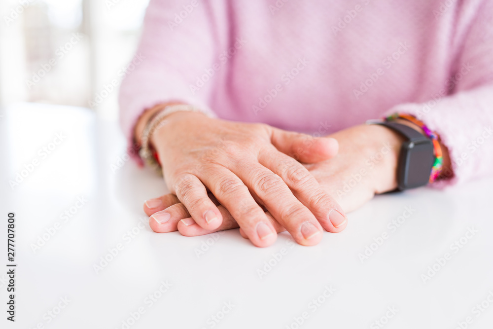 Close up of middle age woman crossed hands over white table Close up of middle age woman crossed hands over white table