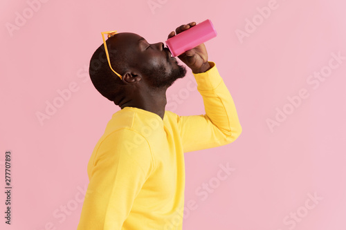 Fototapeta Drink. Black man drinking soft drink on pink background portrait