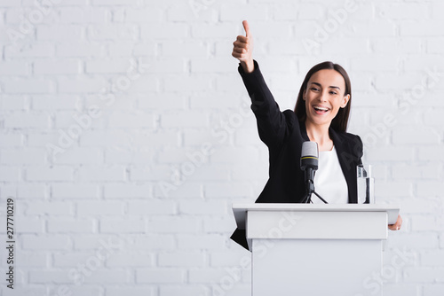 Canvas Print happy, attractive lecturer showing thumb up while standing on podium tribune