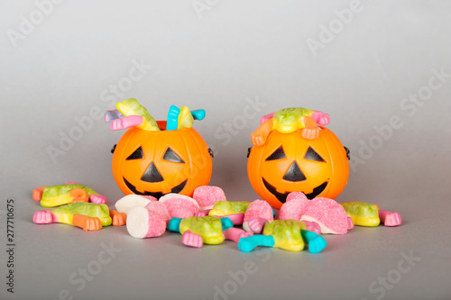 Happy Halloween Trick or Treat jack-o-lantern buckets and pile of colorful sweets candy on gray background. Plastic pumpkins to collect candy.