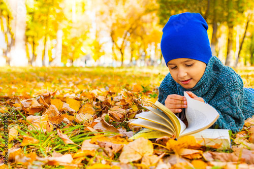 boy lying on his stomach reading a book in the fall in the Park