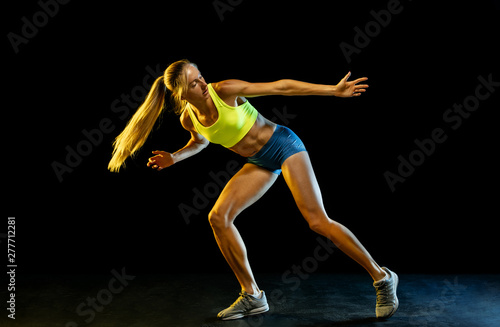 Professional female relay racer training isolated on black studio background in neon light. Woman in sportsuit practicing in running. Healthy lifestyle, sport, workout, motion, action concept.