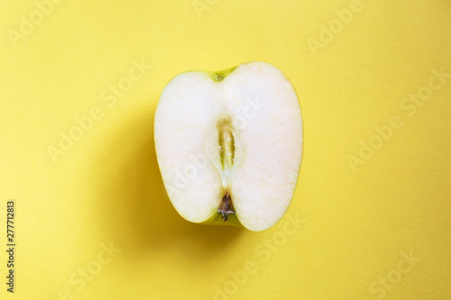 On a yellow monophonic background in the center lies half a green apple. photo