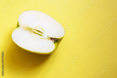 On a yellow monophonic background on the left is half a green apple, on the right there is a place for an inscription