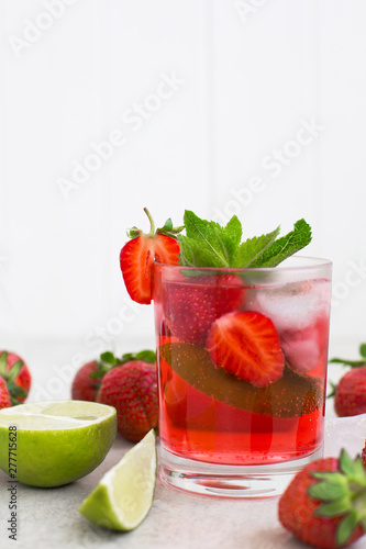 On  gray background there is a strawberry cocktail in a glass with ice and mint and lime
