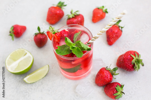 Cooling summer cocktail with strawberries, ice and mint in a glass and around the berries are ripe fresh strawberries and lime