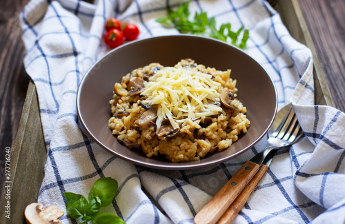 Traditional Italian dish of rice arborio risotto with mushrooms. Served with fresh basil, mushrooms and cherry tomatoes on a dark wooden tray. Close-up