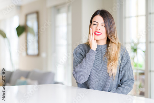 Young beautiful woman wearing winter sweater at home touching mouth with hand with painful expression because of toothache or dental illness on teeth. Dentist concept. Free Download Young beautiful woman wearing winter sweater at home touching mouth with hand with painful expression because of toothache or dental illness on teeth. Dentist concept. - GFXLoad